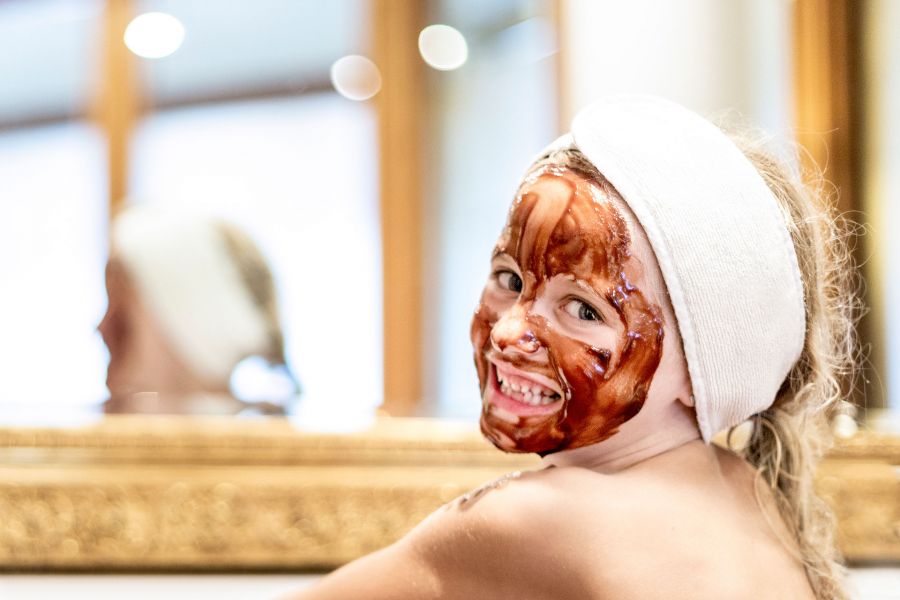 Nahaufnahme eines jungen, grinsenden Mädchens mit einer braunen Gesichtsmaske. Nahaufnahme eines jungen, grinsenden Mädchens mit einer braunen Gesichtsmaske.