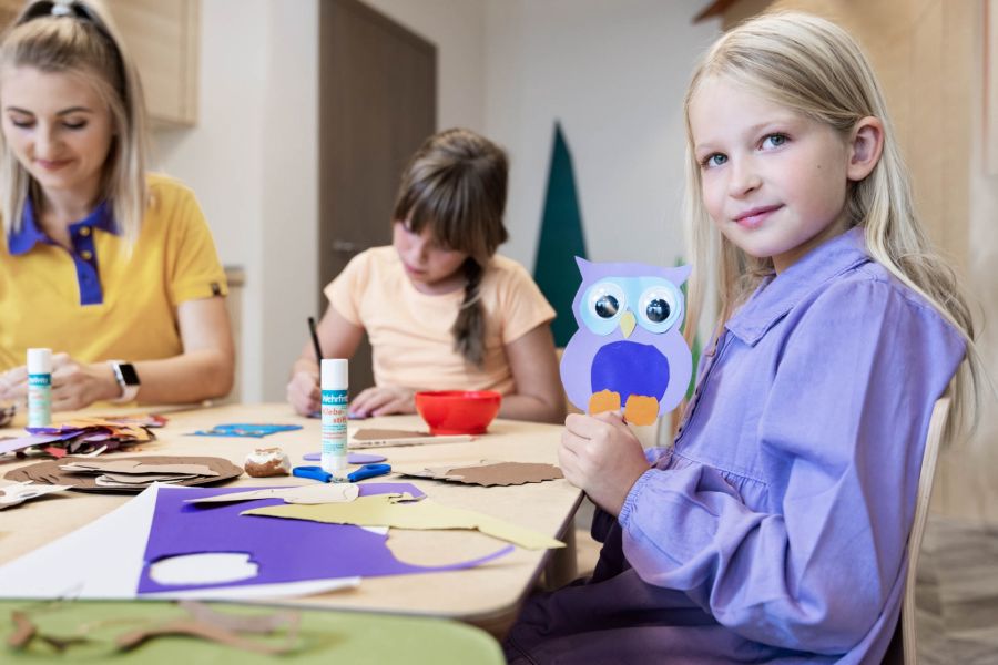 Ein Mädchen am Basteltisch zeigt stolz ihre selbstgebastelte Eule aus Pappe in die Kamera. Ein Mädchen am Basteltisch zeigt stolz ihre selbstgebastelte Eule aus Pappe in die Kamera.
